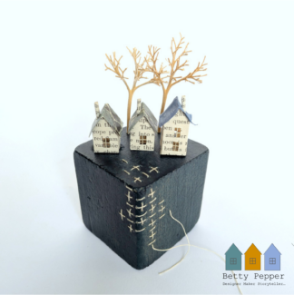 Miniature paper houses handcrafted from faded vintage book covers and book pages, perched on a dark teal vintage child's wooden building block base. This delicate sculpture features hand stitching into the block in a contrast thread. Handmade by British artist Betty Pepper.
