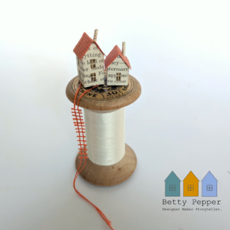 Handmade paper house sculpture on​ a vintage wooden cotton reel with green thread and a tiny black thread ladder by artist Betty Pepper.