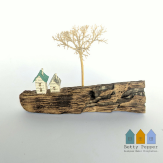 Miniature paper houses handcrafted from faded vintage book covers and book pages, perched on a natural driftwood base. This delicate sculpture features subtle, neutral tones and natural materials by British artist Betty Pepper.