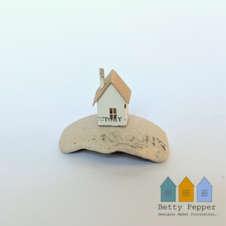 Handmade miniature paper house ​by artist Betty Pepper. Crafted from a recycled book page, mounted on a smooth piece of sea-worn ​p​ottery from a vintage vinegar bottle, displayed against a plain white background.