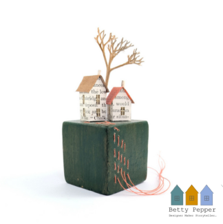 Miniature paper house handcrafted from faded vintage book covers and book pages, perched on a green vintage child's wooden building block base. The block is embellished with orange stitches. By British artist Betty Pepper.