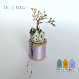 Miniature paper house handcrafted from repurposed book pages perched on a vintage wooden cotton reel wound with beautiful pale lilac thread. A tiny thread ladder hangs down the side of the reel. By British artist Betty Pepper.