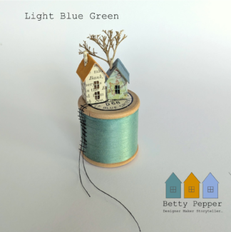 Miniature paper house handcrafted from repurposed book pages perched on a vintage wooden cotton reel wound with beautiful minty aqua thread. A tiny thread ladder hangs down the side of the reel. By British artist Betty Pepper.