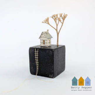 Miniature paper houses handcrafted from faded vintage book covers and book pages, perched on a black vintage child's wooden building block base. A tiny thread ladder hangs down the side of the block. By British artist Betty Pepper.