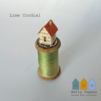 Handmade miniature paper house crafted from a recycled book page, mounted on a vintage wooden cotton reel with 2 tone, lime green thread, displayed against a plain white background.